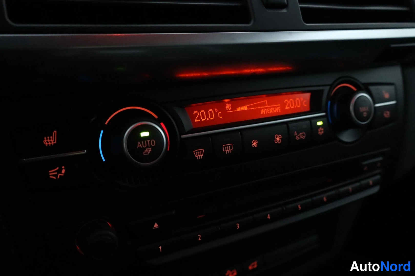 Muu: Auton sisätilan ilmastointipaneeli punaisella näytöllä, jossa lukee 20.0°C ja INTENSIVE, AUTO-napaa ympäröi vihreä valo.