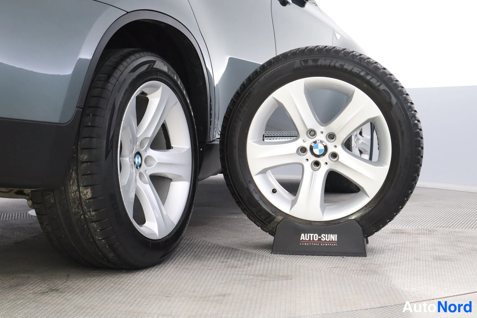 Sivulta: BMW:n takapyörä hopeavanteella ja vieressä Auto-Sunin tolkalla seissyt vara-Michelin-renkas;
