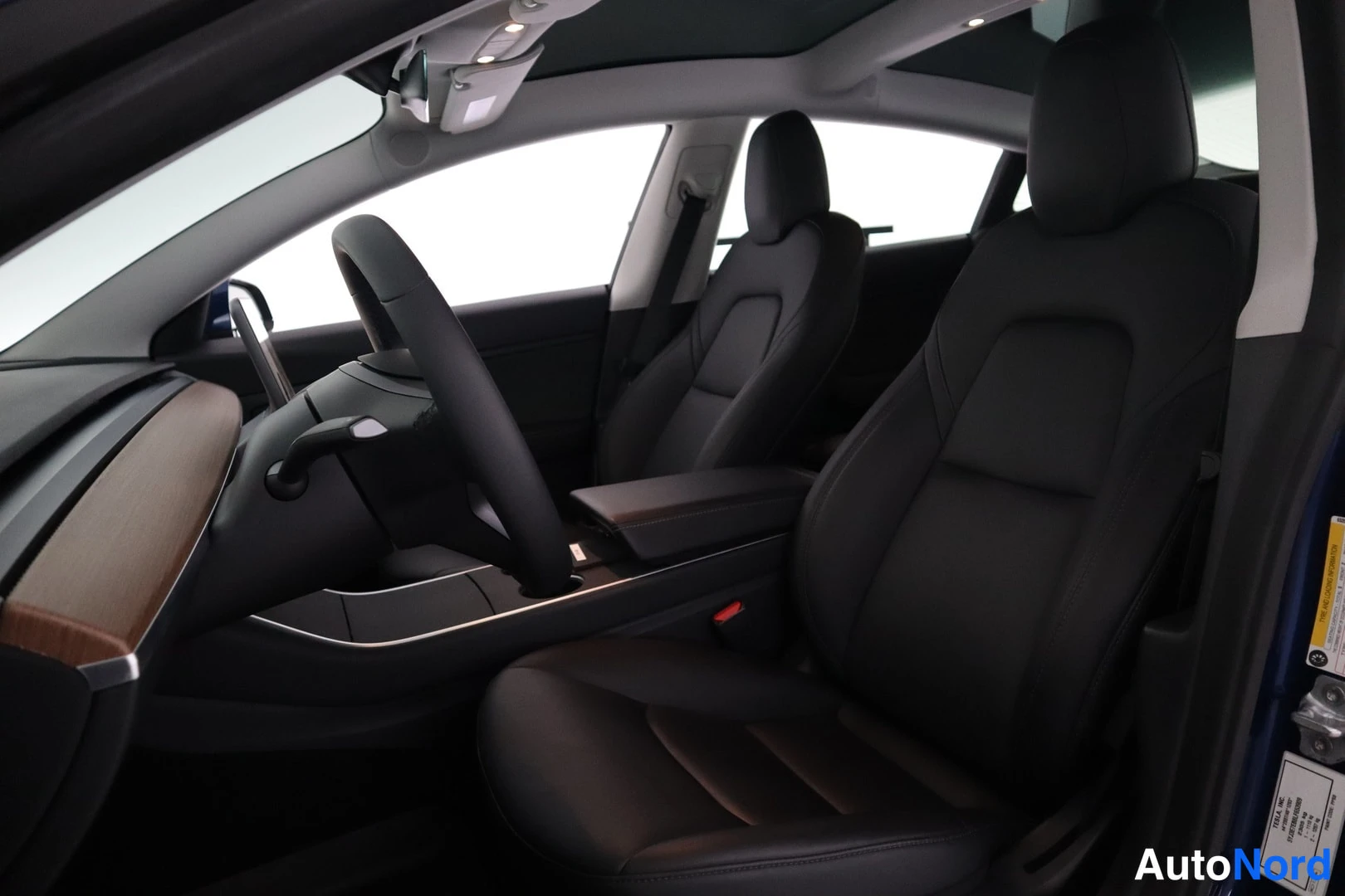 Muu: Tesla-automallin sisätilat kuljettajan puolelta: ohjauspyörä, mustat istuimet ja paneelikatto.