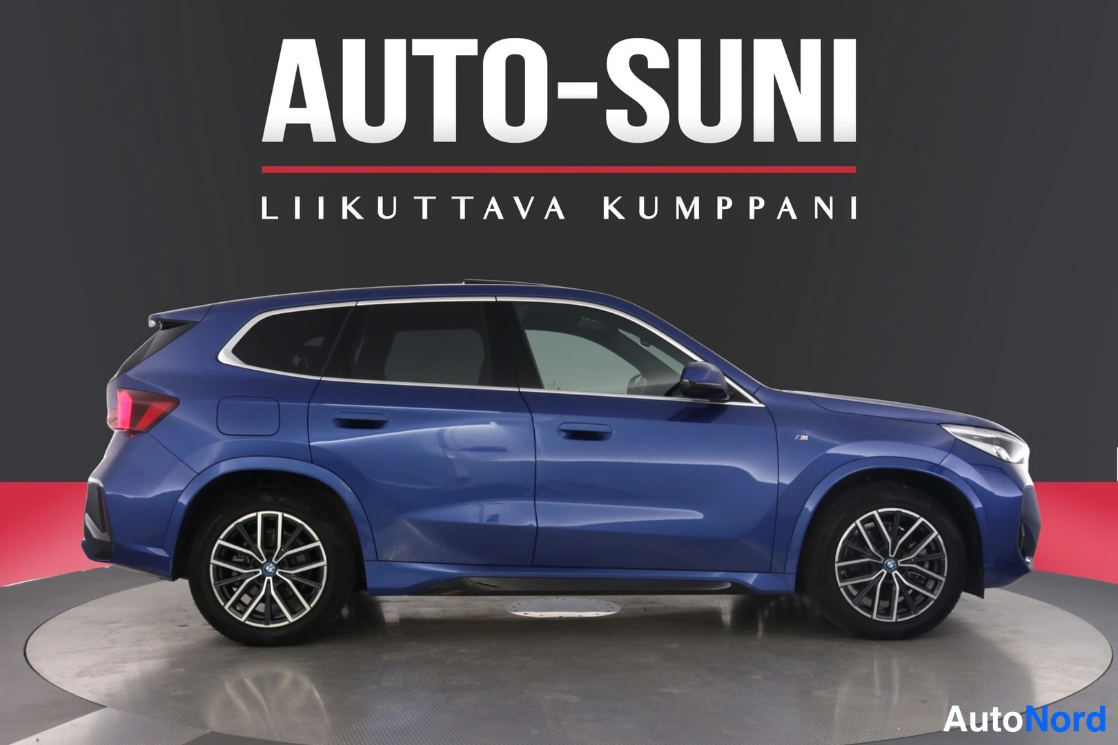 Sivulta: Sininen BMW iX1 sivuprofiilista myyntihallissa.