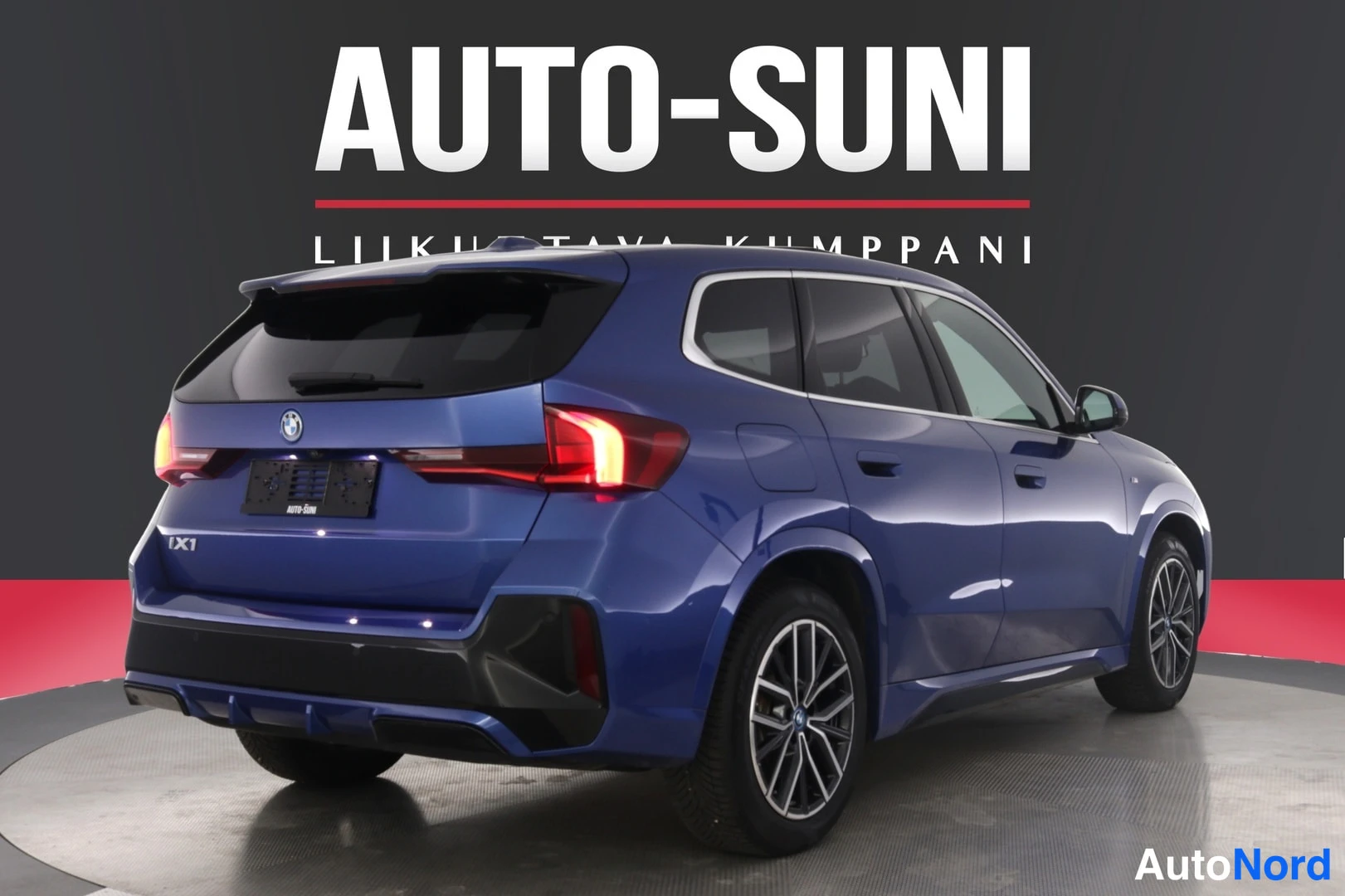Takaviisto: Sininen BMW iX1 takakulmanäkyvissä, takavalo sytytettynä.
