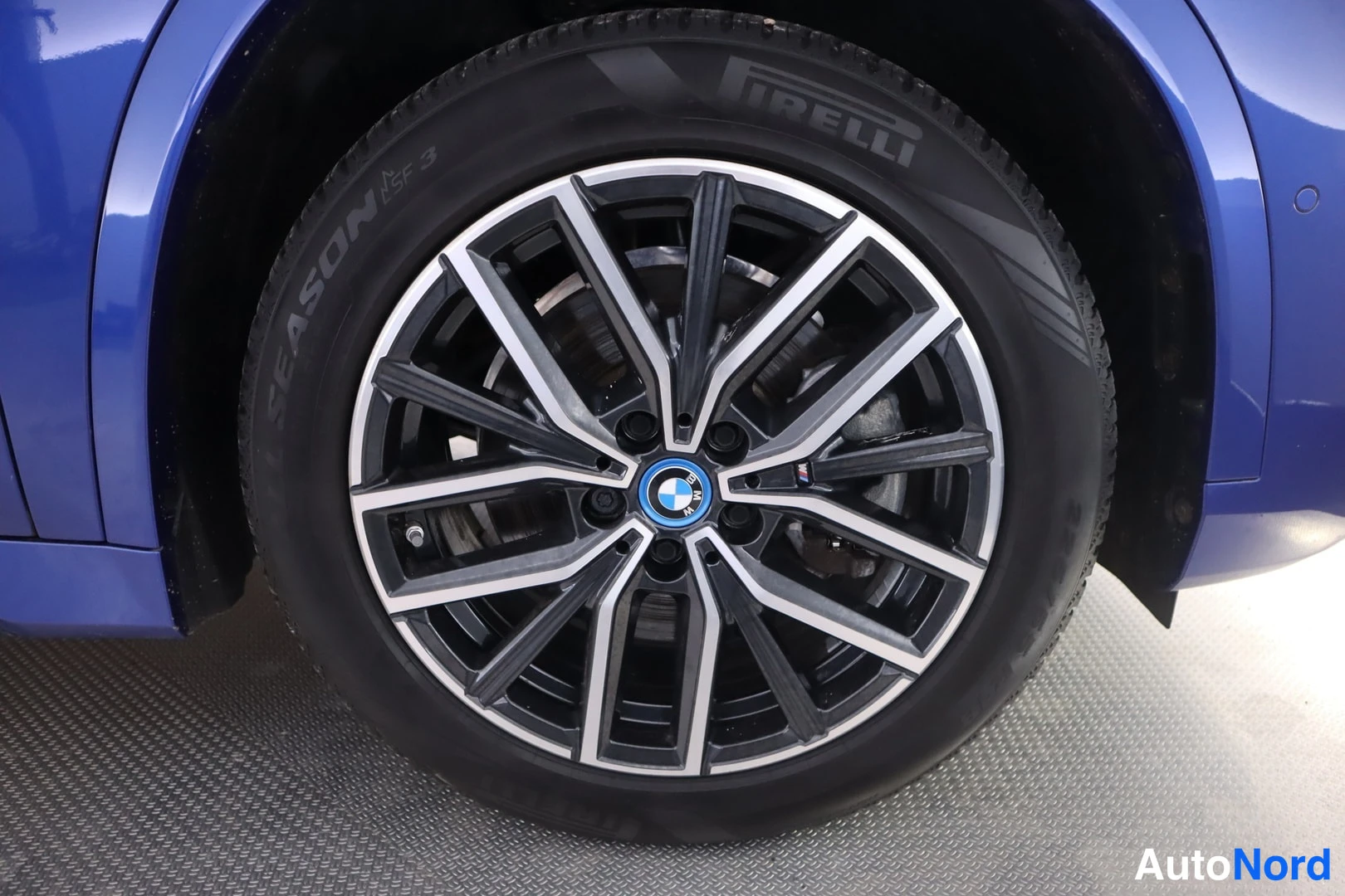 Yksityiskohta: Sinisen auton kevytmetallivanne ja Pirelli Season -rengas lähikuvassa, BMW:n merkki napassa.