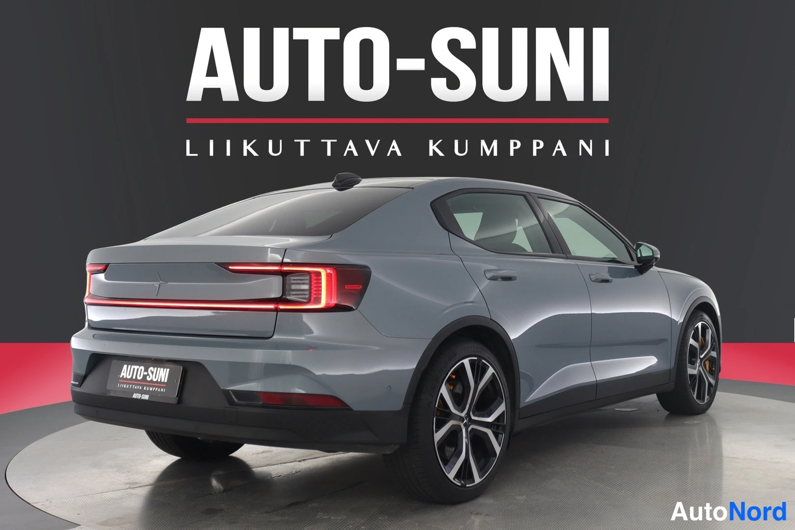 Takaviisto: Sinertävänharmaan henkilöauton takaosa ja oikea kylki näyttelylavalla, punainen valokoru perävaloissa.