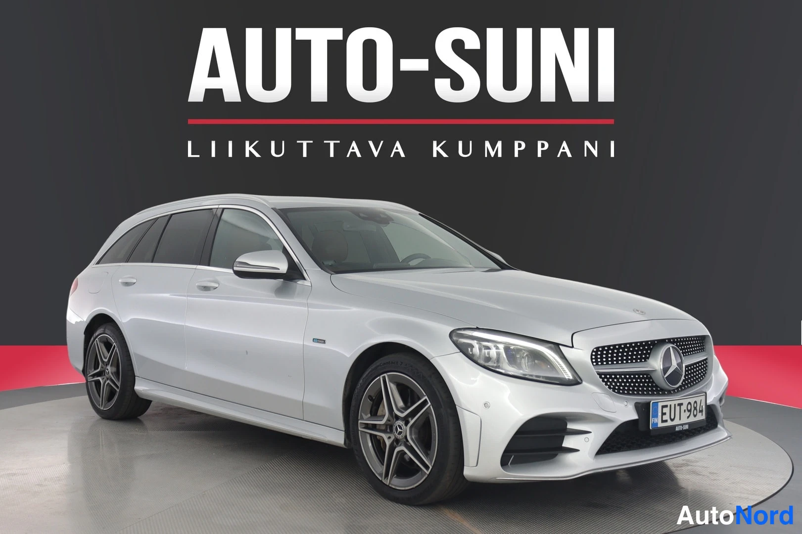 Etuviisto, nokka oikealle: Hopeanvärinen Mercedes-Benz C -farmari kulmassa edestä, AMG-tyyppiset vanteet ja rekisterikilpi.