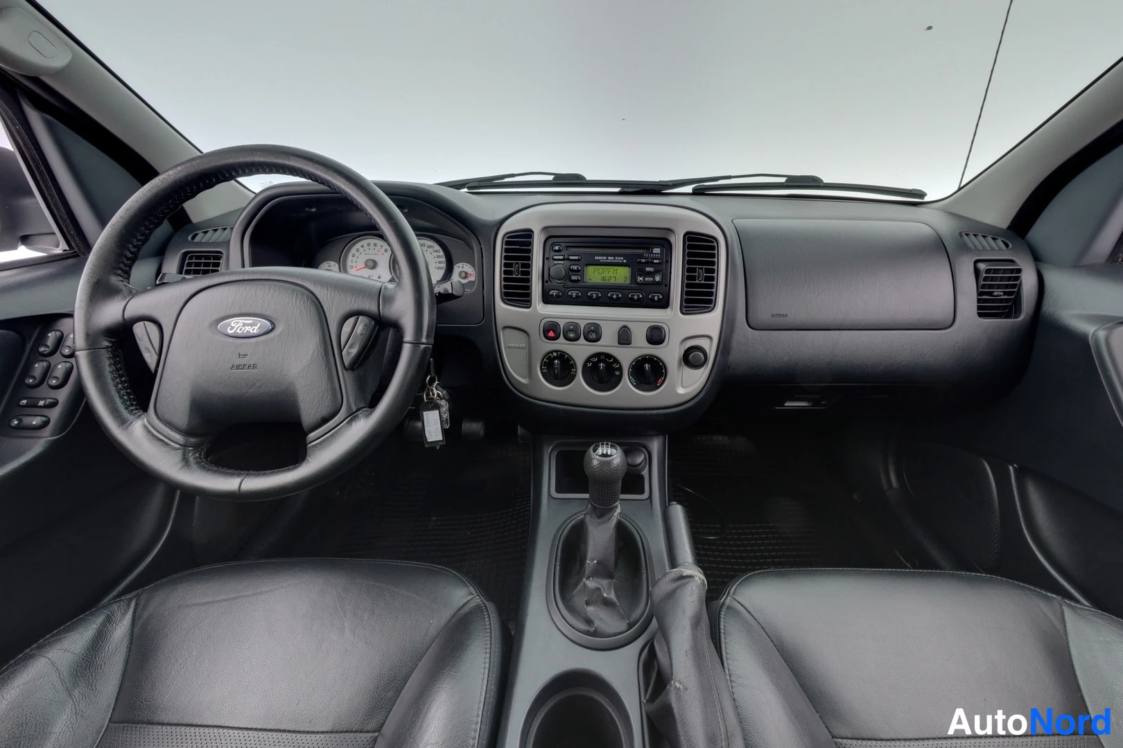 Muu: Ford Maverickin ohjaamo etusisätilasta: Ford-ohjauspyörä, manuaalivaihteen keila, radioyksikkö ja mustat nahkaistuimet.