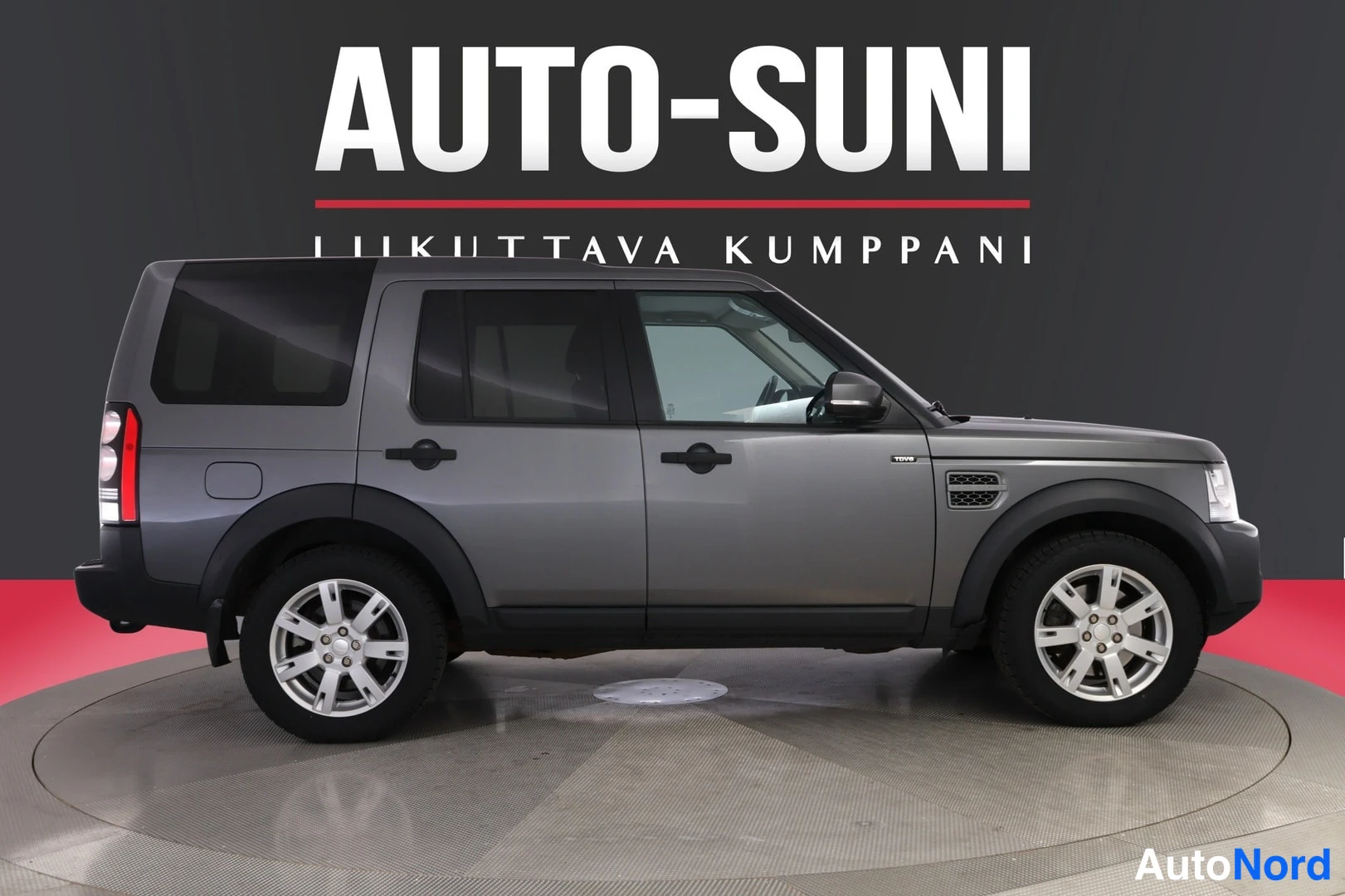 Sivulta: Auto-Sunin taustaa vasten auton sivu profiilissa: harmaa farmarikori neljällä ovella, vasen kylki ja takavalot osittain näkyvissä.