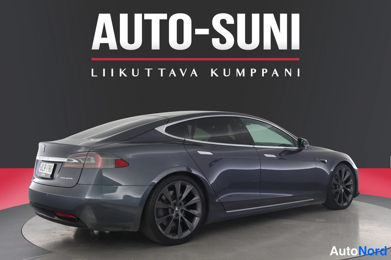Takaviisto: Tummanharmaa Tesla Model S takaosa kolmannelta kulmalta, perä ja kylki näkyvissä, rekisterikilpi.