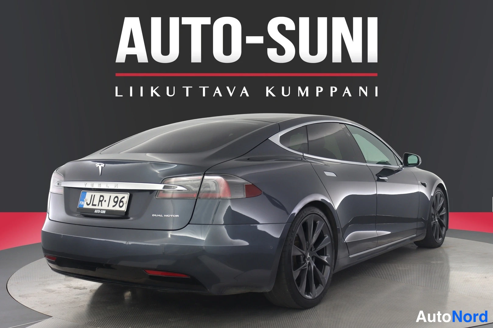 Takaviisto: Tummanharmaa Tesla Model S takaa yläviistosta, perä ja kylki näkyvissä, rekisterikilpi, DUAL MOTOR -teksti perässä.