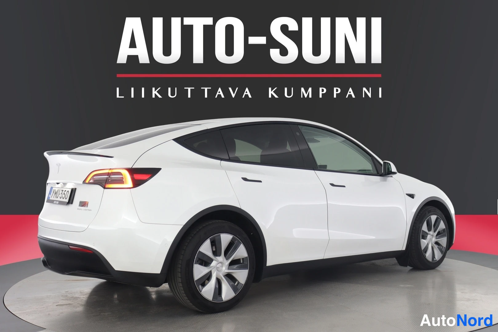 Takaviisto: Valkoinen Tesla Model Y takaviistokuva studiossa, rekisteritunnus YM U-350 näkyvissä, taustalla AUTO-SUNI-kyltti.