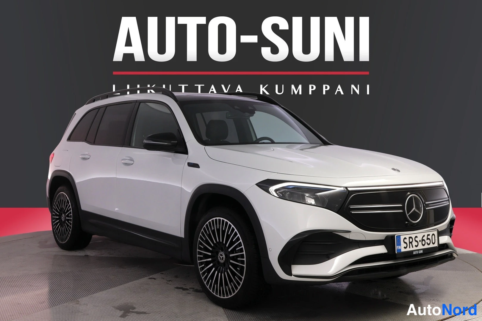 Etuviisto, nokka oikealle: Valkoinen Mercedes-Benz EQB edestä oikealta kuvattuna studio-ympäristössä, rekisteritunnus, musta katto ja kevytmetallivanteet.