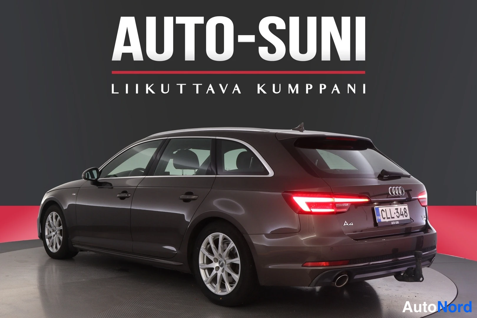 Takaviisto: Auton takaosa ja vasen kylki, rekisterikilpi, taustalla mainoskyltti.