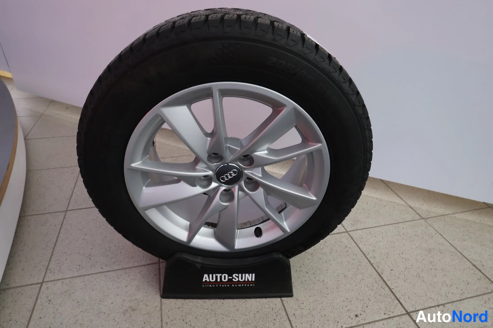 Yksityiskohta: Audi-merkkinen hopeinen alumiinivanne mustalla renkaallaAuto-Suni-näyttelytelineessä sisätiloissa.