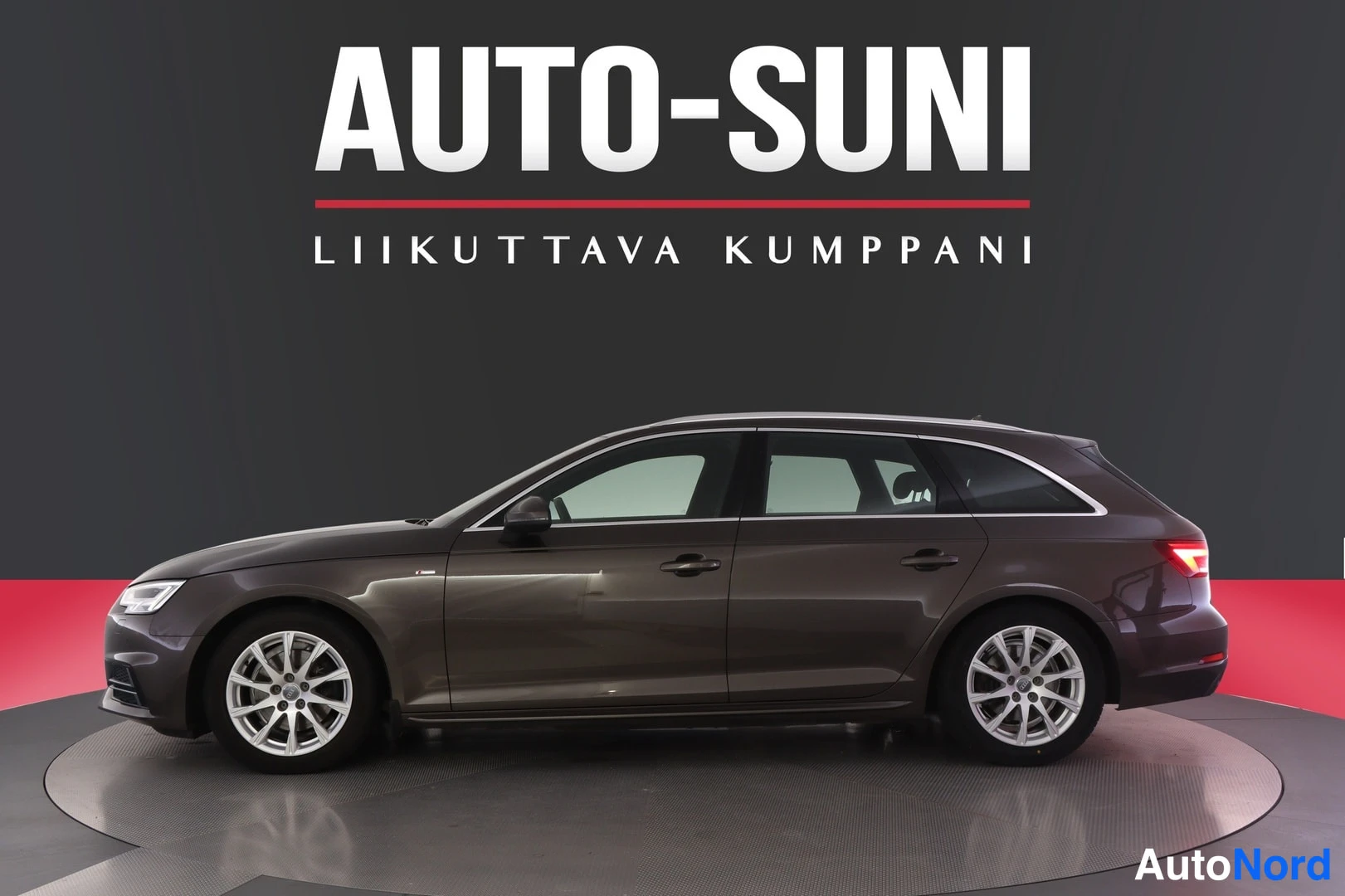 Etuviisto: Auton etuosa ja vasen kylki hallintatilassa, taustalla mainoskyltti.