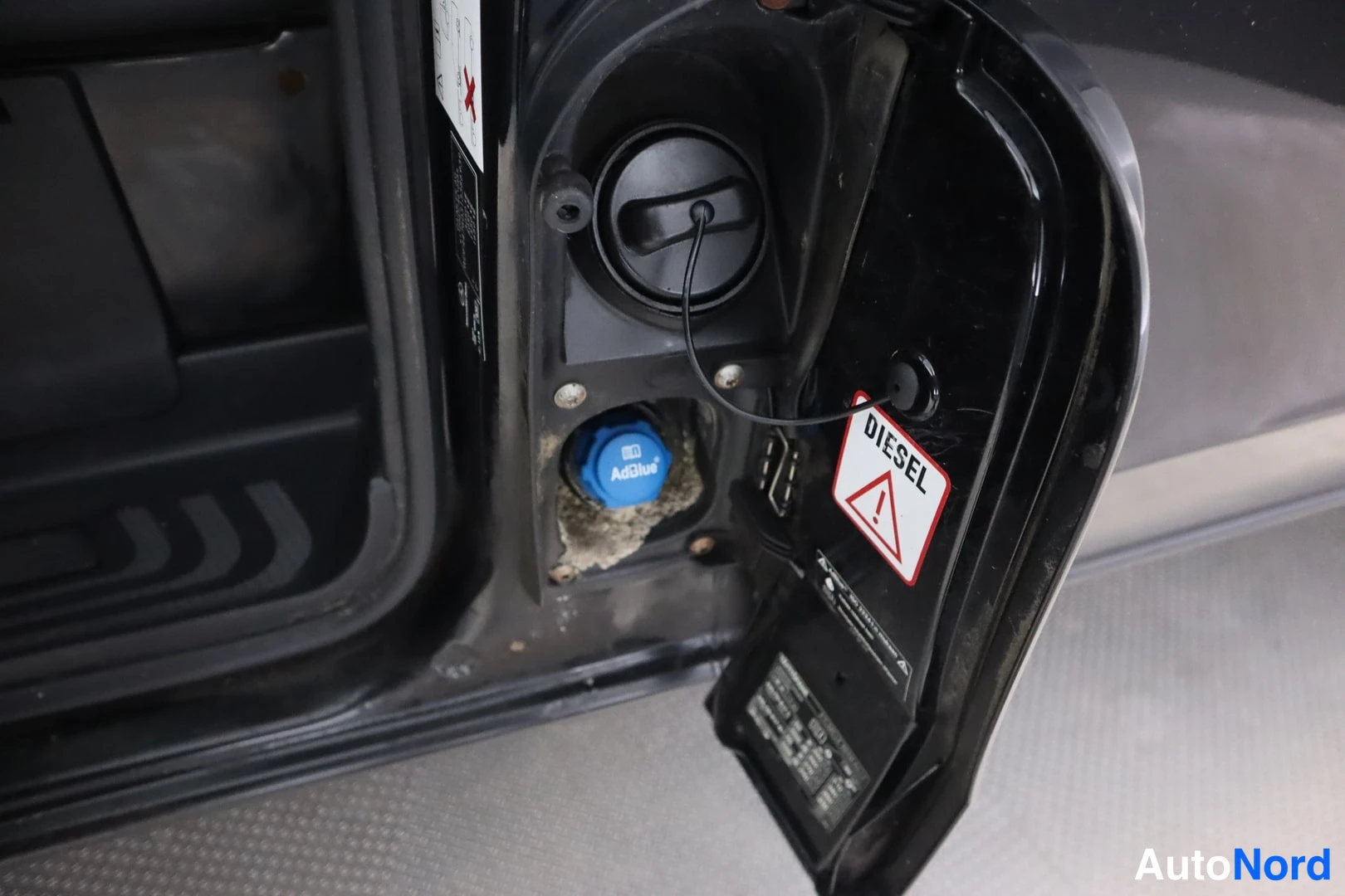 Yksityiskohta: Polttoainetäytön suu auki, kannessa DIESEL-varoitusmerkki ja vieressä sininen AdBlue-säiliön korkki.