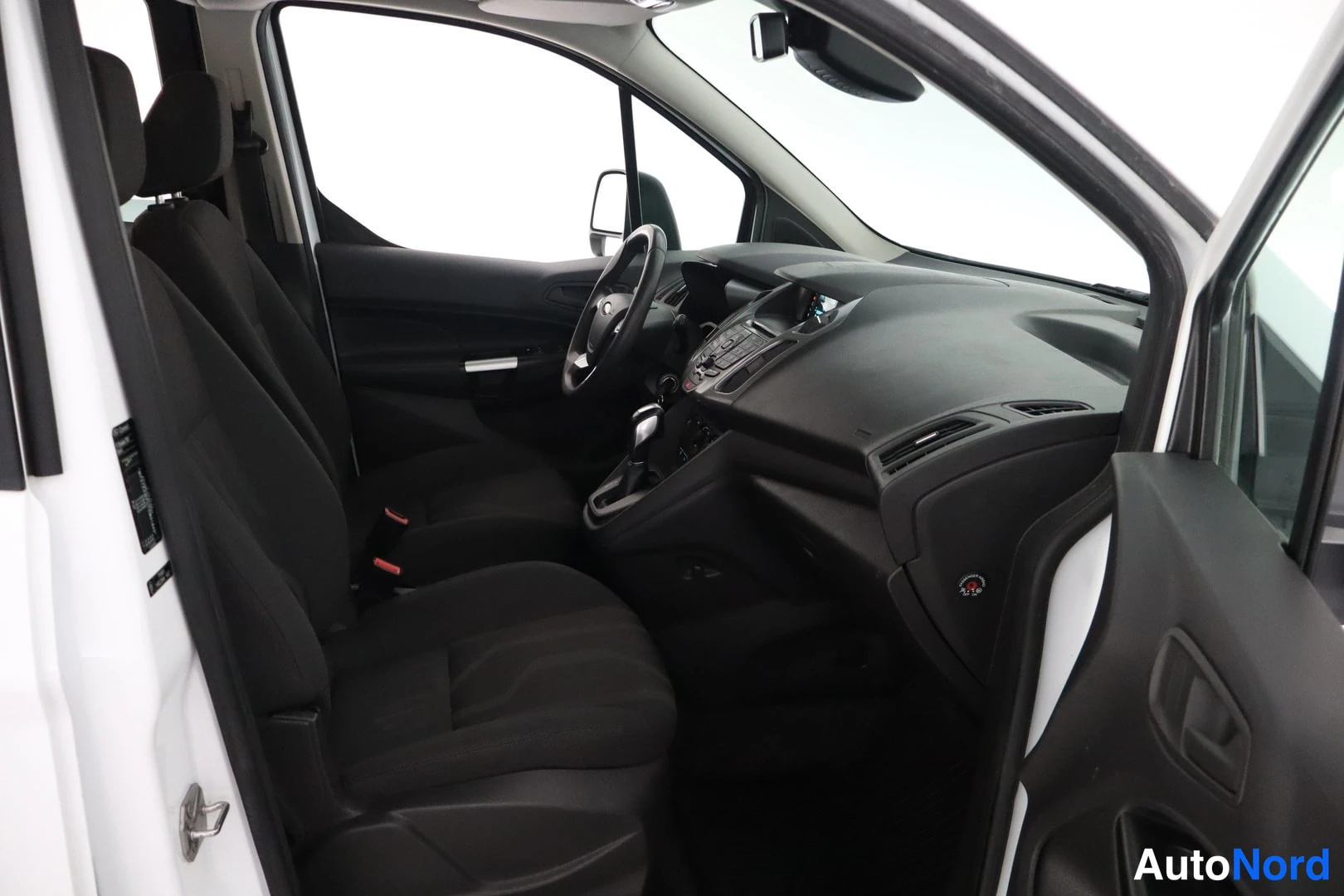 Muu: Ford Tourneo Connectin etusohja: tumma tekstiilipenkit, ohjauspyörä, automaattivaihteisto ja kojelauta näkyvät avoimesta oikeasta etuovesta.