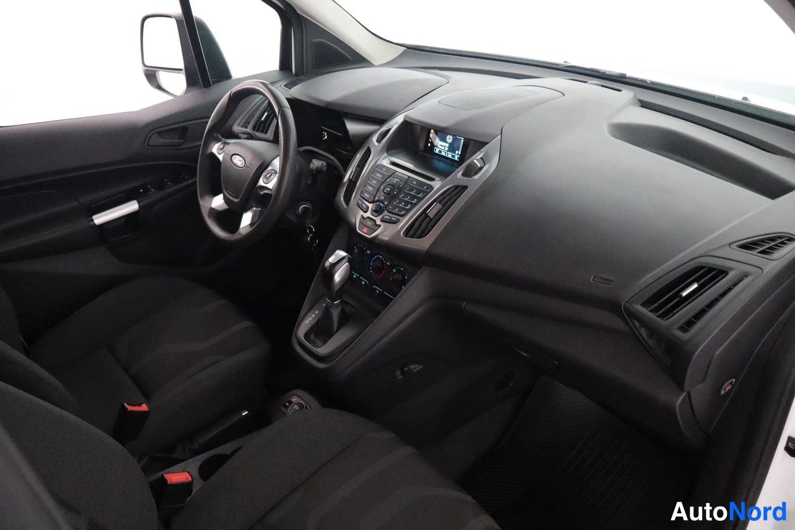 Muu: Ford Tourneo Connectin ohjaamo ylhäältä: tumma kojelauta, Ford-ohjauspyörä, automaattivalitsin ja keskinäyttö.