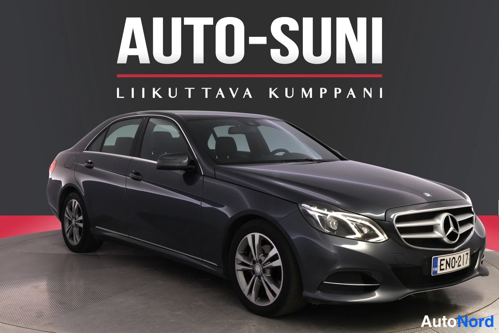 Etuviisto, nokka oikealle: Mercedes-Benz E-sedanin etukulmanäkyvys tummanharmaana, rekisterikilpi.