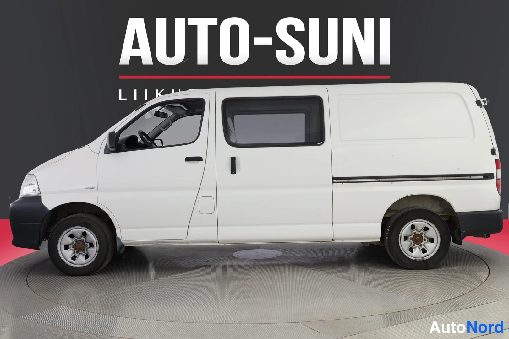 Sivulta: Sivukuva valkoisesta Toyota Hiace -pakettiautosta studiossa, tumma tausta ja punainen lattia.
