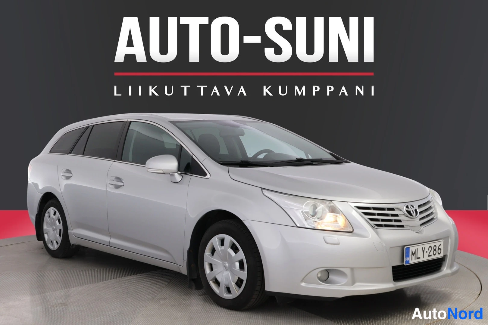 Etuviisto, nokka oikealle: Hopeanvärinen farmariauto vinosti etuviistosta kuvattuna, etusäleikkö ja ajovalot näkyvät, rekisteritunnus.