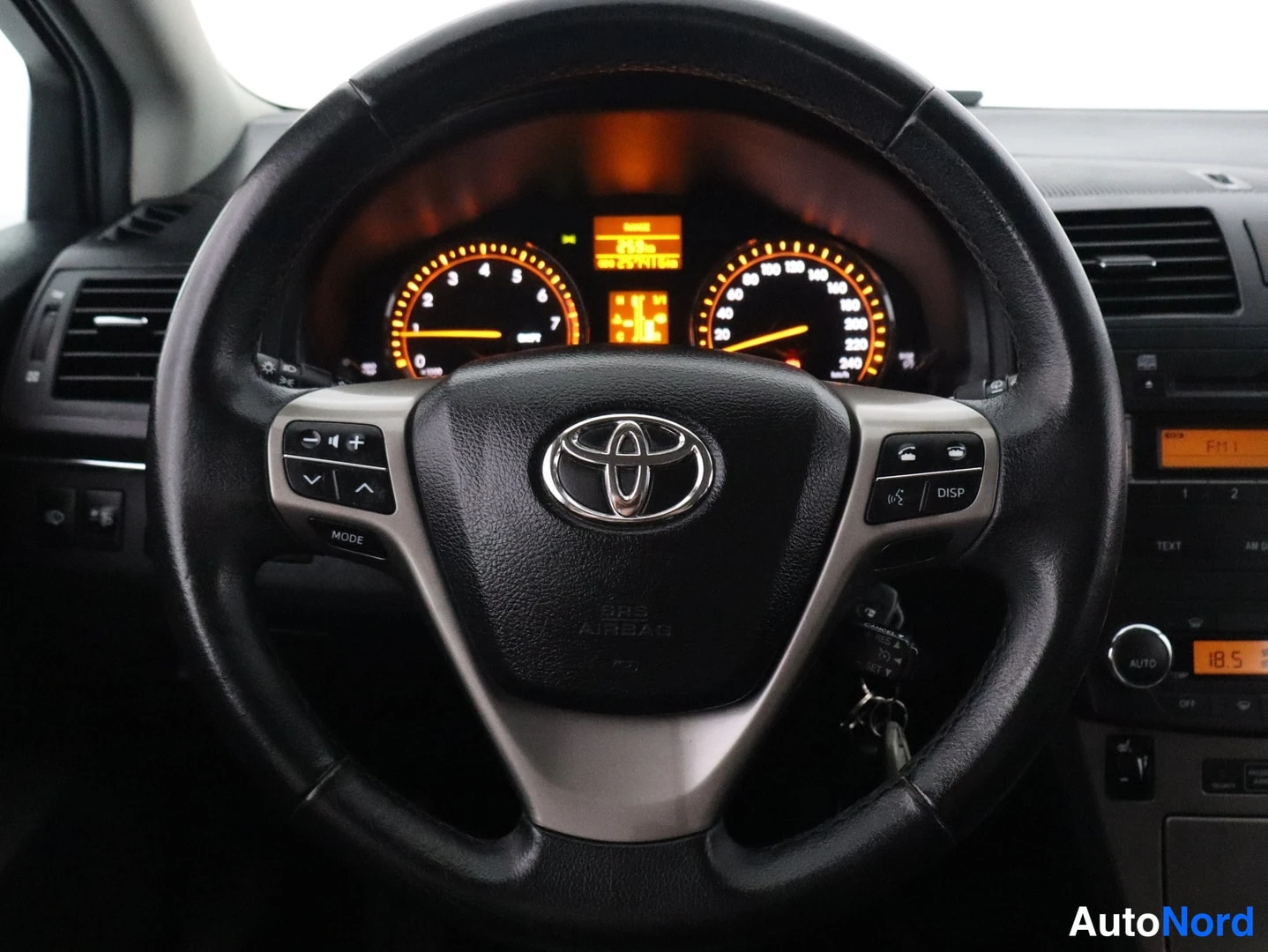 Muu: Toyota Avensisin ohjauspyörä Toyota-tunnuksella; pyörän napeilla ääniohjaimet (MODE, DISP), taustalla mittarit ja kojelaudan näytöt.