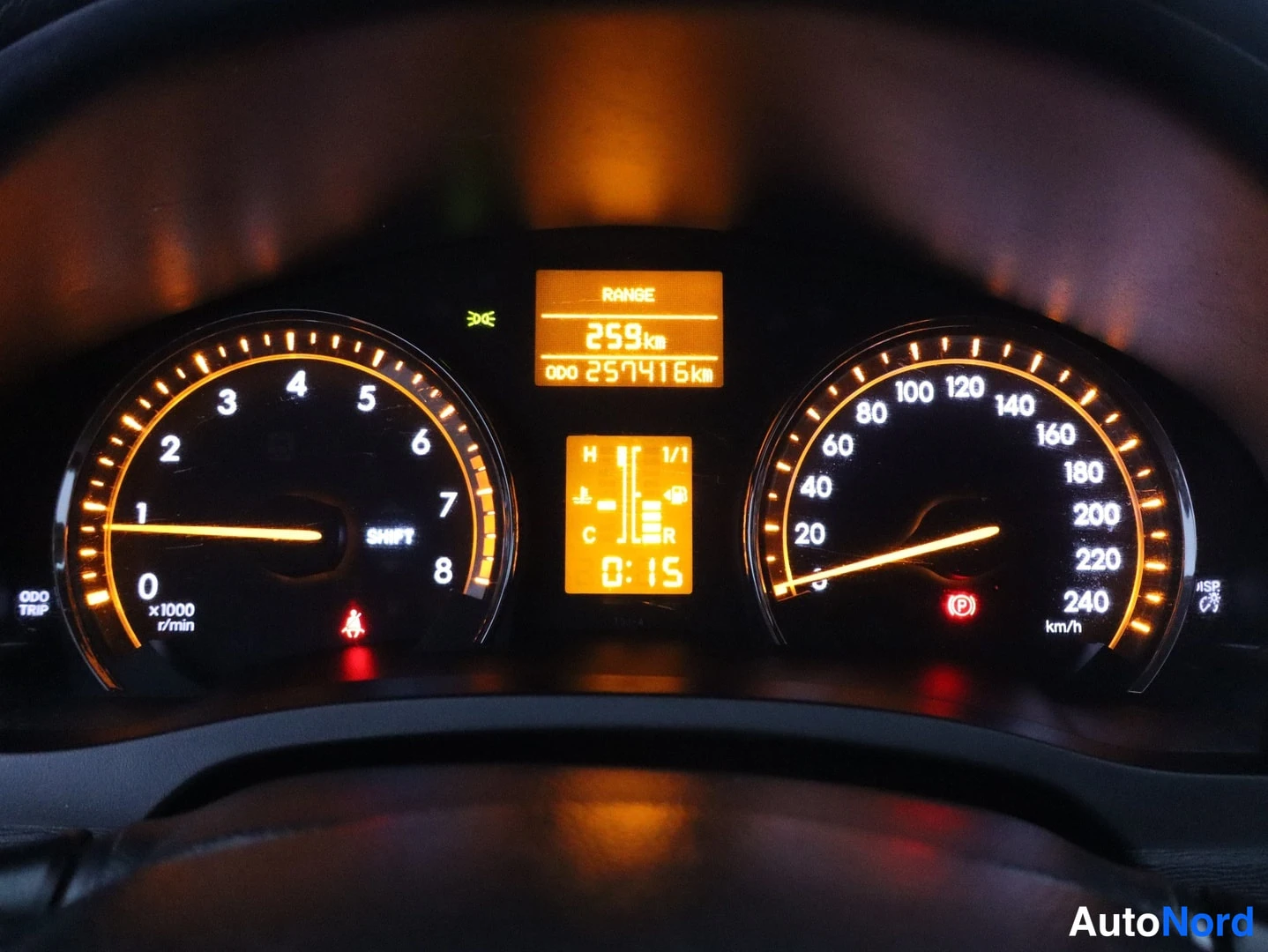 Muu: Toyota Avensisin mittaristo yövalaistuksessa; näytössä lukema 257416 km ja RANGE 259 km. Kuva tarkka, mutta lasista heijastuu hehkua.