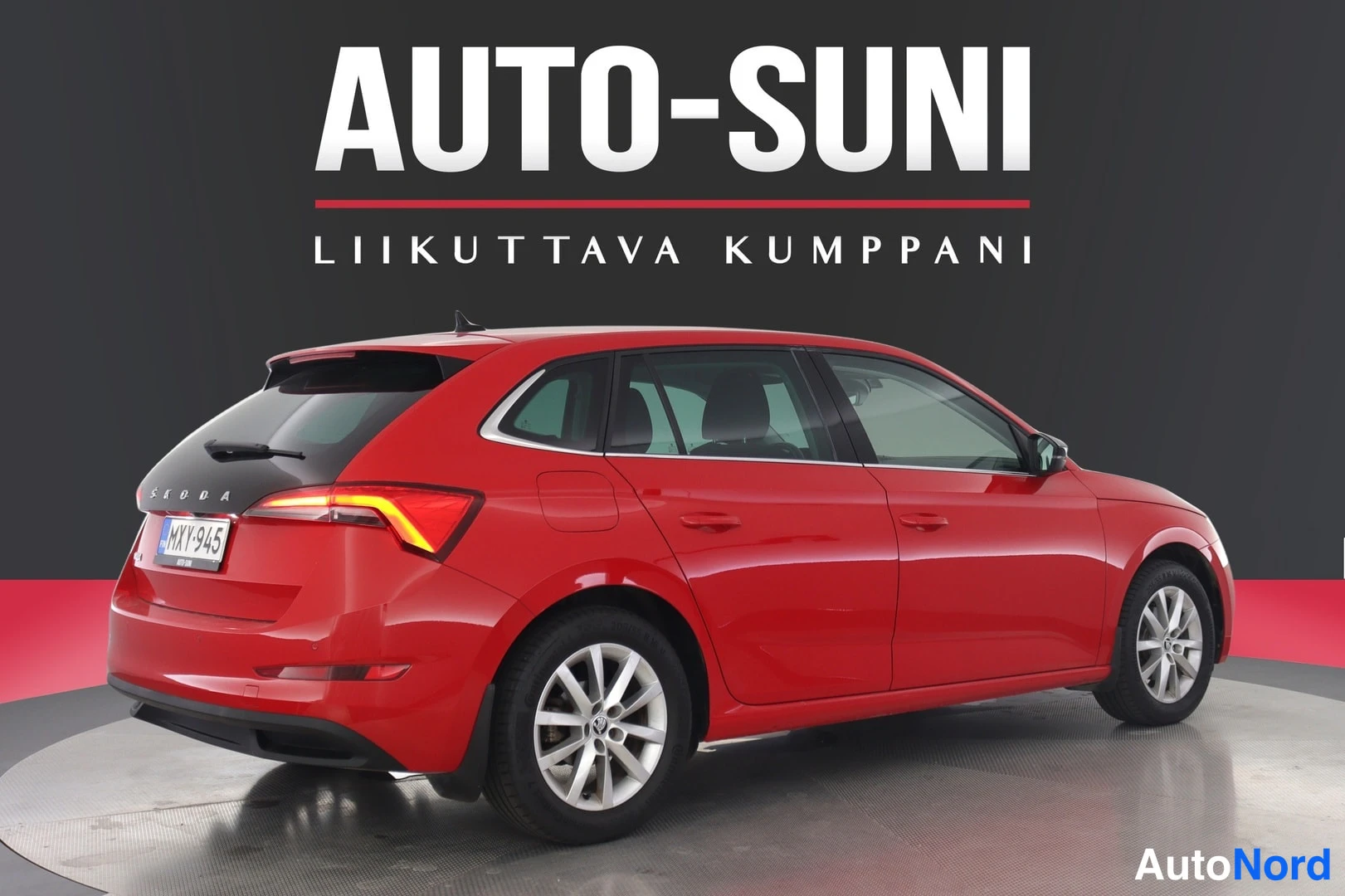 Takaviisto: Punaisen Skoda Scalan takaosa ja sivuprofiili studiotreffissä, rekisterikilpi, takavalot taustavalossa.