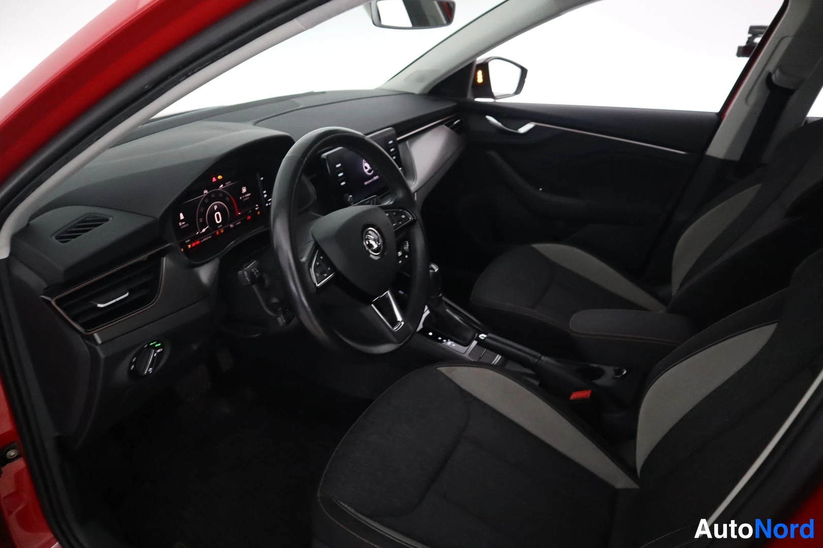Muu: Autoon näkyy sisäpuolelta kuljettajan puolelta: Skoda-tunnuksellinen tasko, digitaalinen mittaristo, keskinäyttö ja automaattivaihteen valitsin.