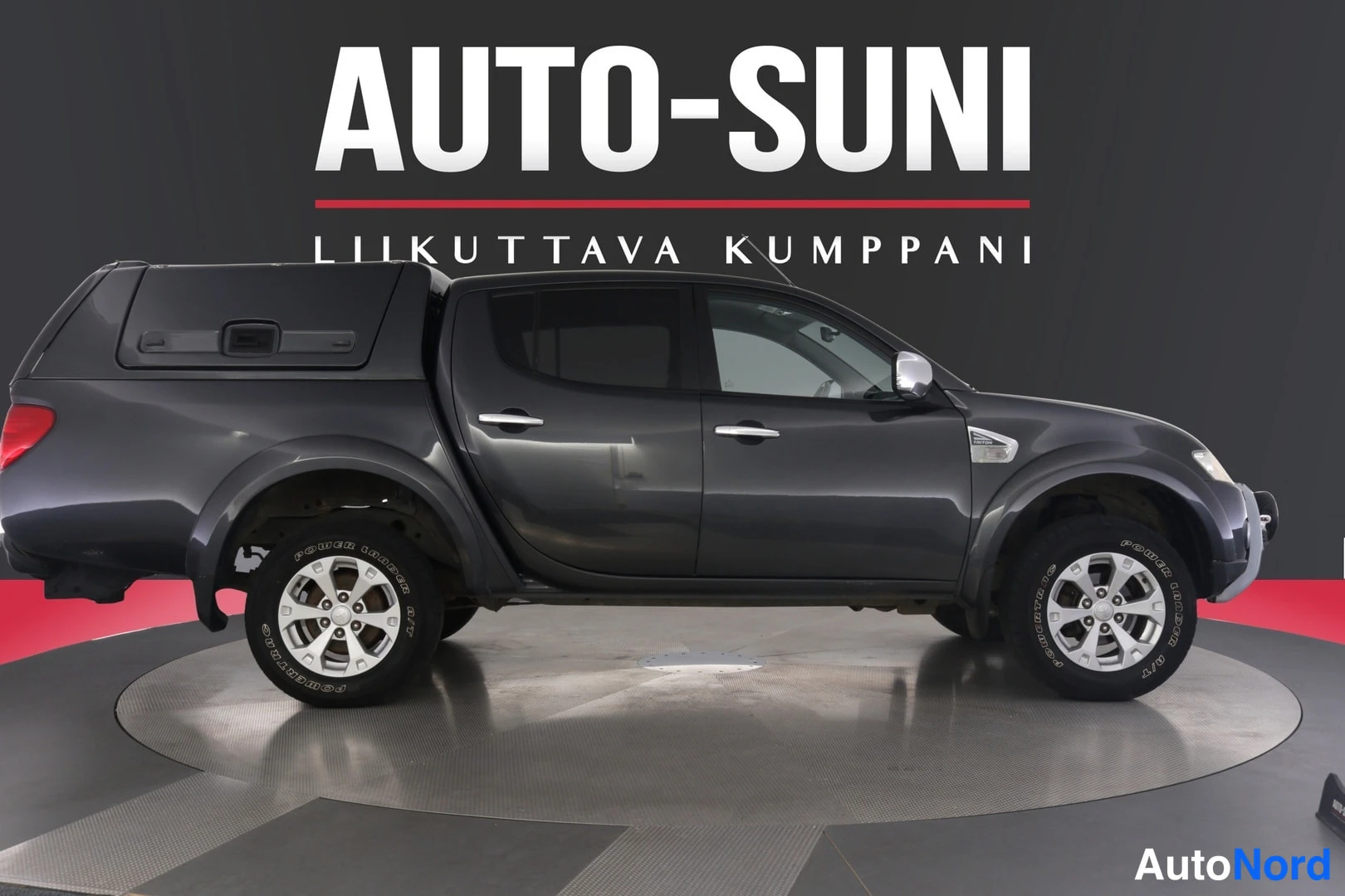 Sivulta: Mitsubishi L200 -mallin tummanharmaan avolava-auton sivuprofiili oikealta nähtynä, lavassa tumma kuormakoppi.