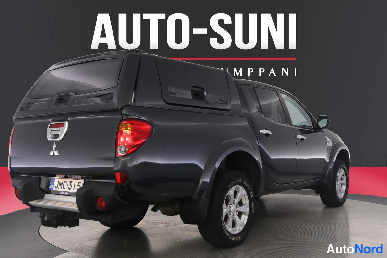 Takaviisto: Mitsubishi L200 -mallin tummanharmaa avolava-auto kulmassa takaa vasemmalta nähtynä, rekisteritunnus.