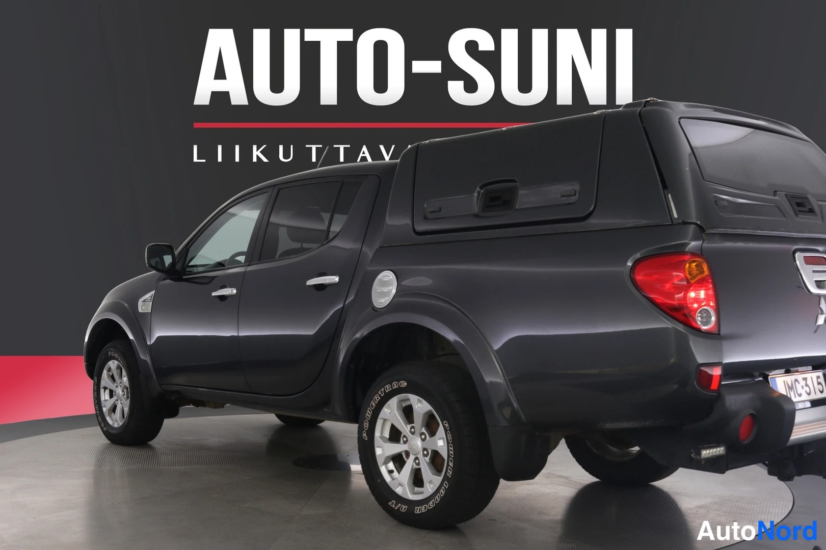 Takaviisto: Mitsubishi L200 -mallin tummanharmaa avolava-auto kulmassa takaa oikealta nähtynä, lavassa tumma kuormakoppi.