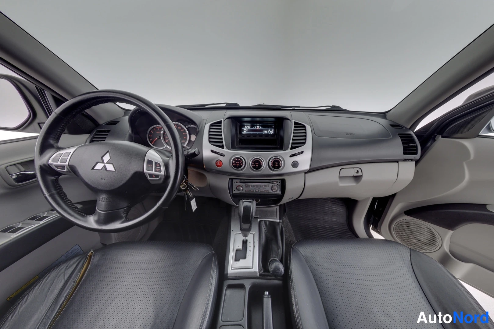 Etuistuimet: Mitsubishin ohjaamo suoraan edestä: Mitsubishi-merkkinen ratto, automaattivaihtevinvalitsin ja infotainment-näyttö keskikonsolissa