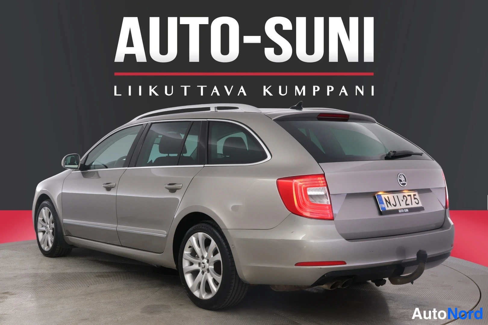 Takaviisto: Hopeanvärinen farmariauto takaviistosta studiossa, yllä Auto-Sunin mainosbanneri.