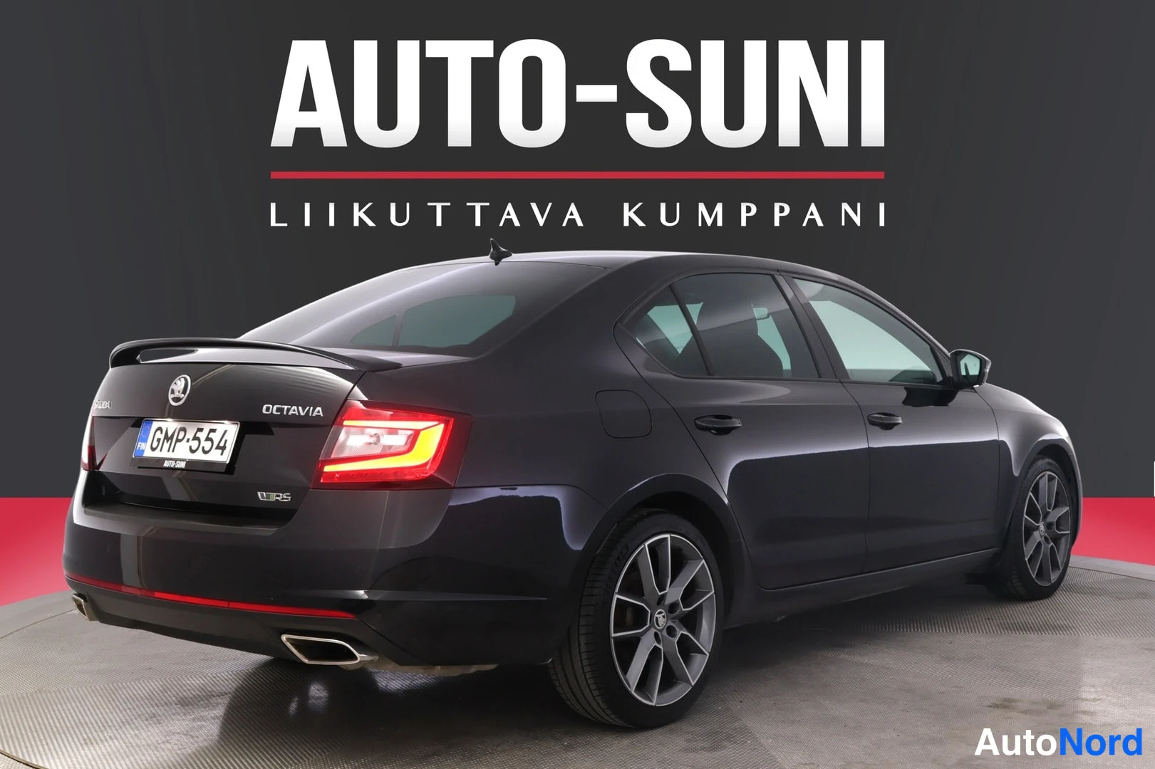 Takaviisto: Musta auto takakolmannelta näkyvältä, takavalojen tummat lasit syttyneenä punaisena.