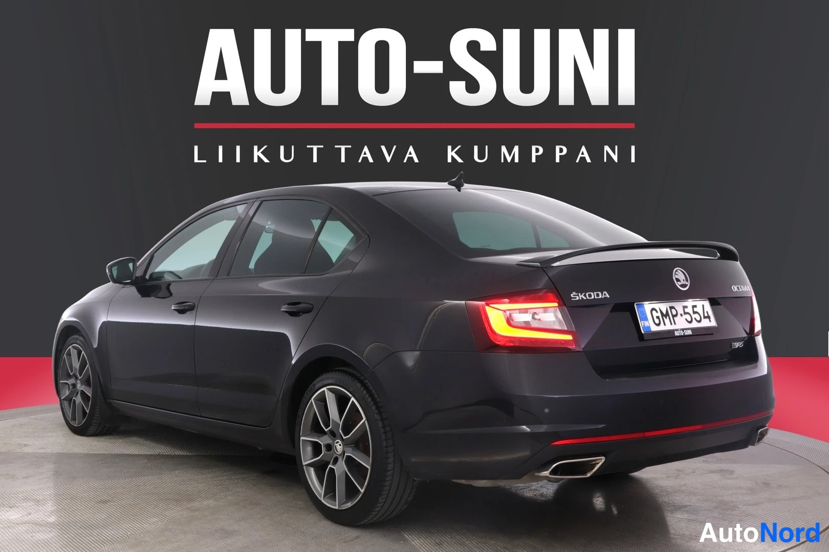 Takaviisto: Musta auto takakolmannelta näkyvältä, punaiset heijastimet takapuskissa.