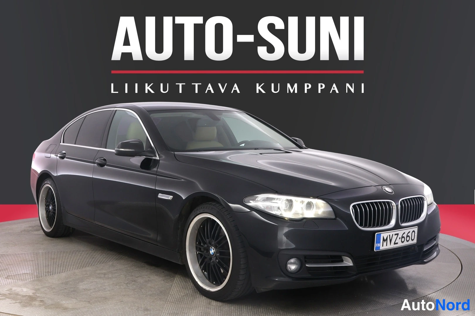 Etuviisto, nokka oikealle: Mustan BMW-sedanin etukolmesivukuva studiotyökalussa, rekisterikilpi, taustalla AUTO-SUNI-logo.