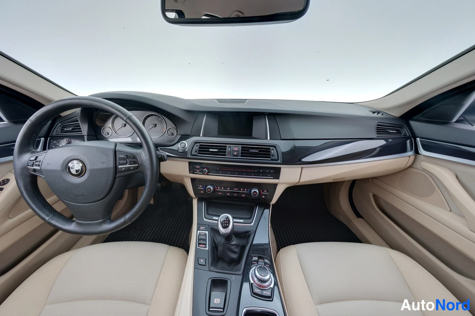 Yksityiskohta: BMW:n ohjaamo: beige istuimet, monitoimapöytä ja keskikonsolin manuaalivaihtokeila
