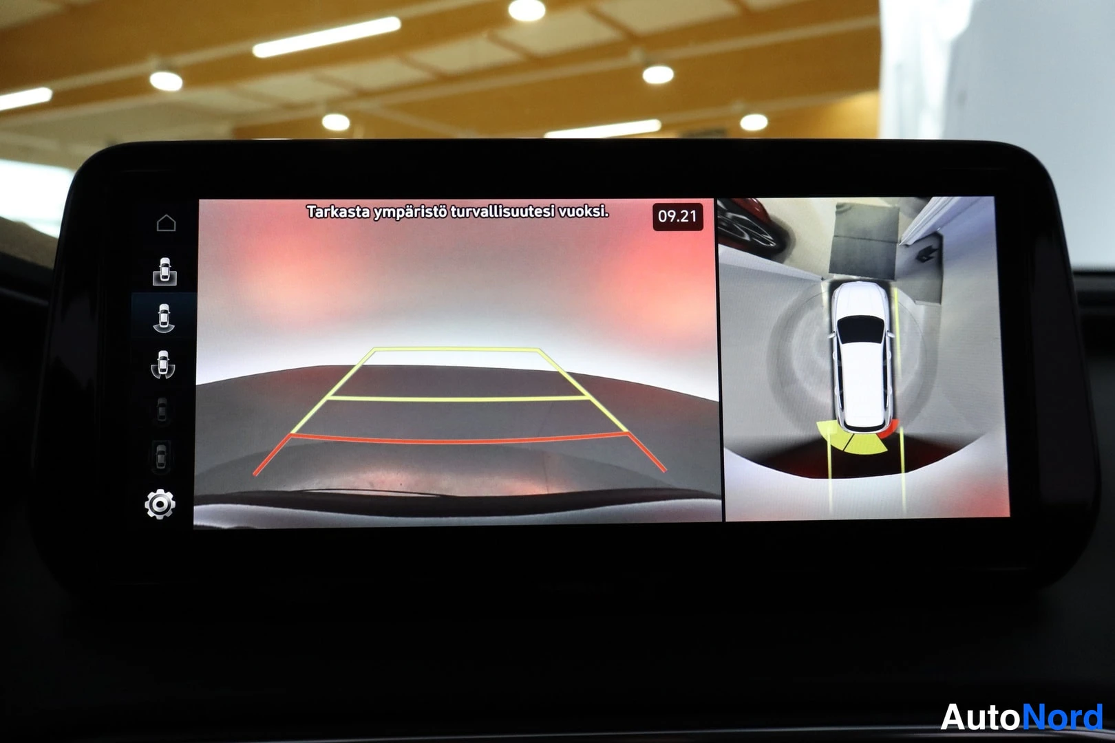 Muu: Infotainment-näytöllä kamera-apu: peruutuskamera ohjausviivoineen ja ylinäkymä autosta.