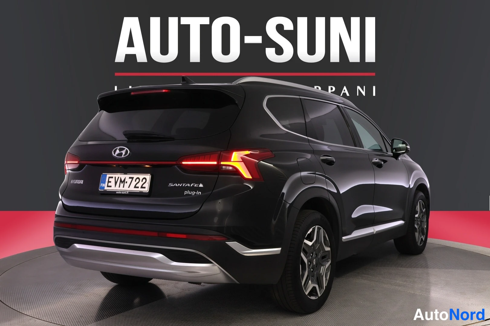 Takaviisto: Mustan SUV-auton takakulma-näkymä, jossa näkyy takavalot, rekisteritunnus ja tekstit SANTA FE plug-in, autosalon myyntikuvassa.