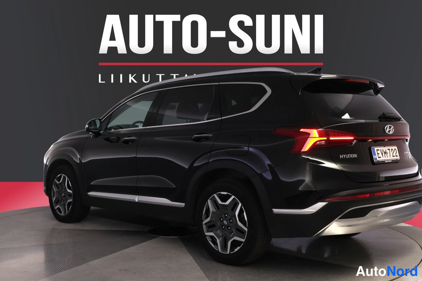 Takaviisto: Mustan SUV-auton takakulma-näkymä vasemmalta, jossa näkyy takavalot, rekisteritunnus ja HYUNDAI-teksti, autosalon myyntikuvassa.