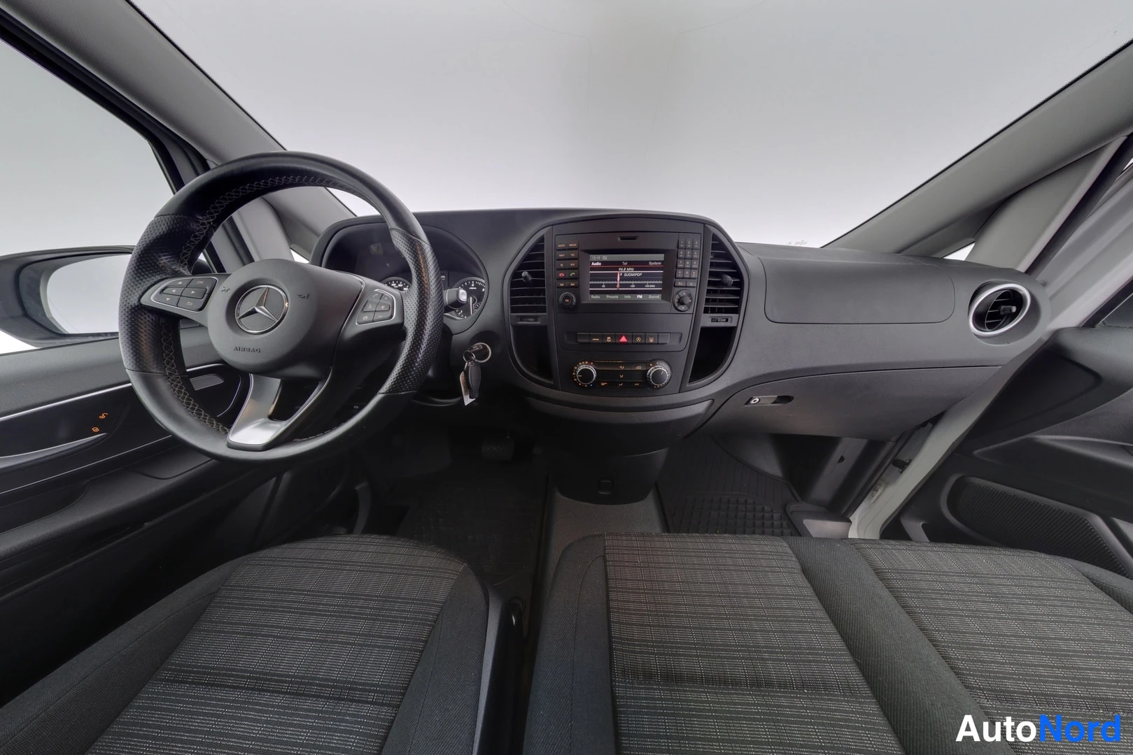 Muu: Mercedes-Benz Vito -pakettiauton ohjaamo: Mercedes-merkillä varustettu ohjauspyörä, kojelauta ja keskikonsolissa radio/näyttöyksikkö.