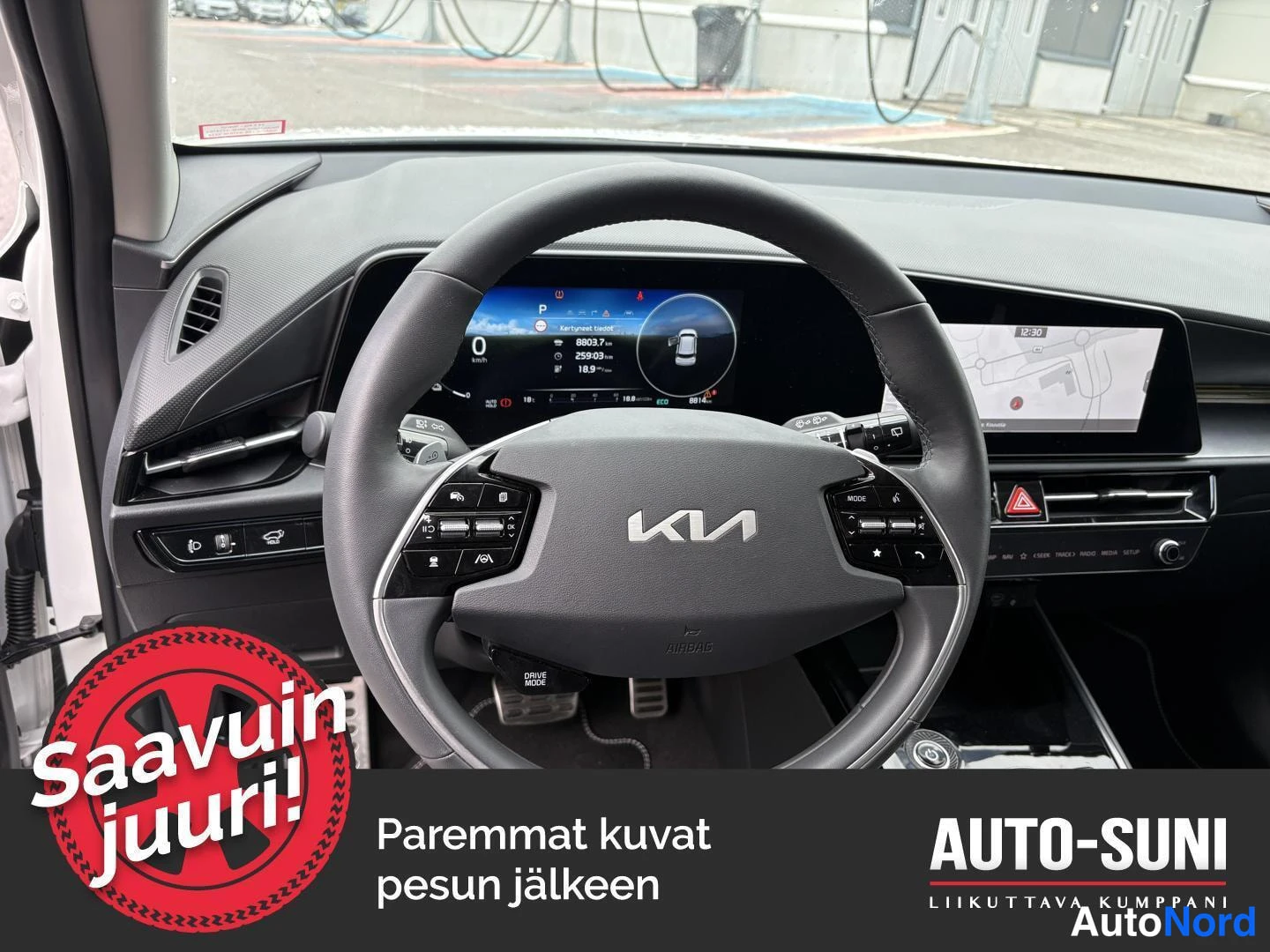 Edestä: Kuljettajan näkymä Kia-merkkisen auton ohjaamoon: multitoimintainen ohjauspyörä, digitaalinen mittaristo ja keskinäyttö näkyvät; autonometriä näyttää 8003,7 km.