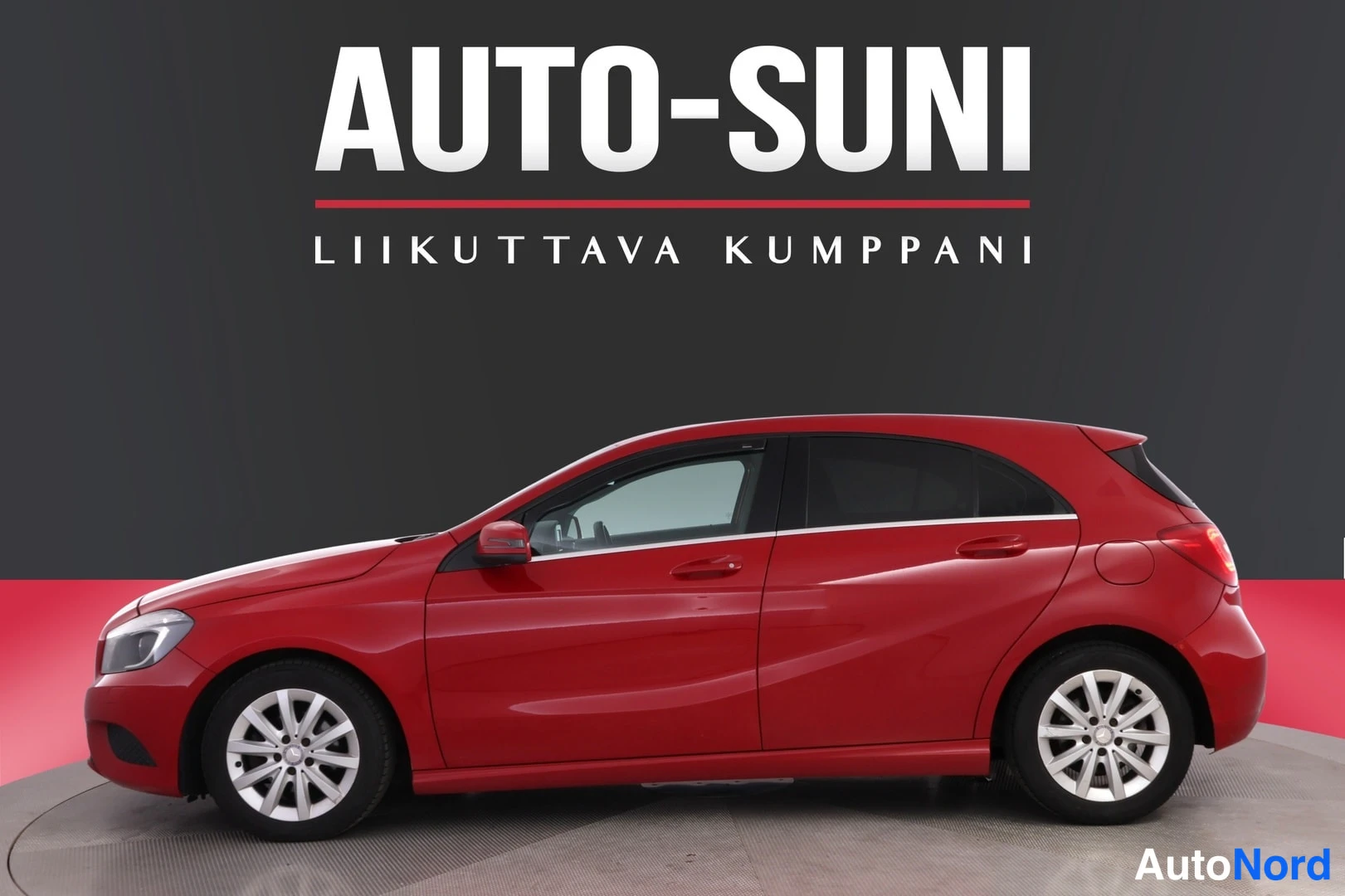 Sivulta: Punainen Mercedes-Benz A -henkilöauto sivulta vasen keula, Auto-Suni mainosbanneri taustalla