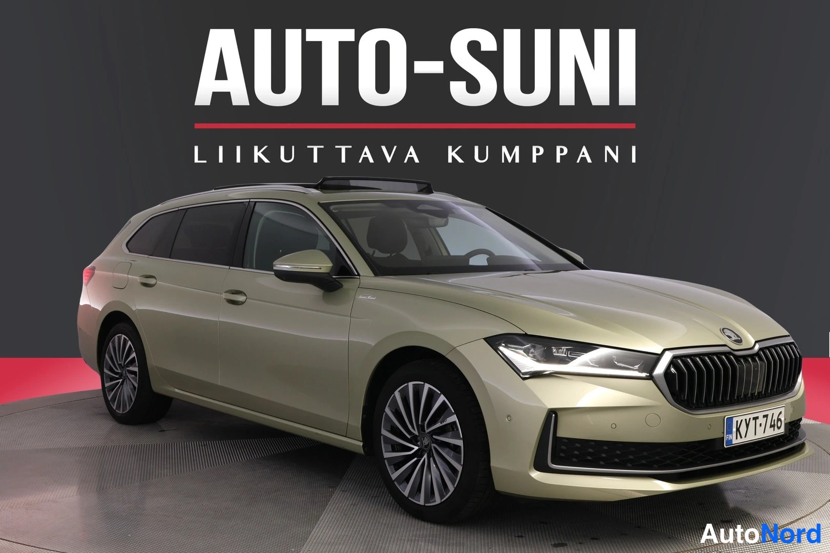 Etuviisto, nokka oikealle: Kultaanvärisen Skoda Superb -farmarin etukulma näkyy studiotaulussa, rekisteritunnus, AUTO-SUNI-tunnus taustalla.