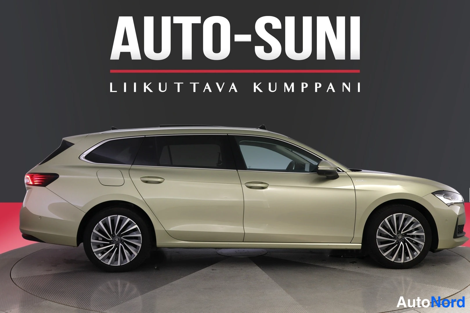 Sivulta: Kultaanvärisen Skoda Superb -farmarin sivuprofiili studiotaulussa, AUTO-SUNI-tunnus taustalla.