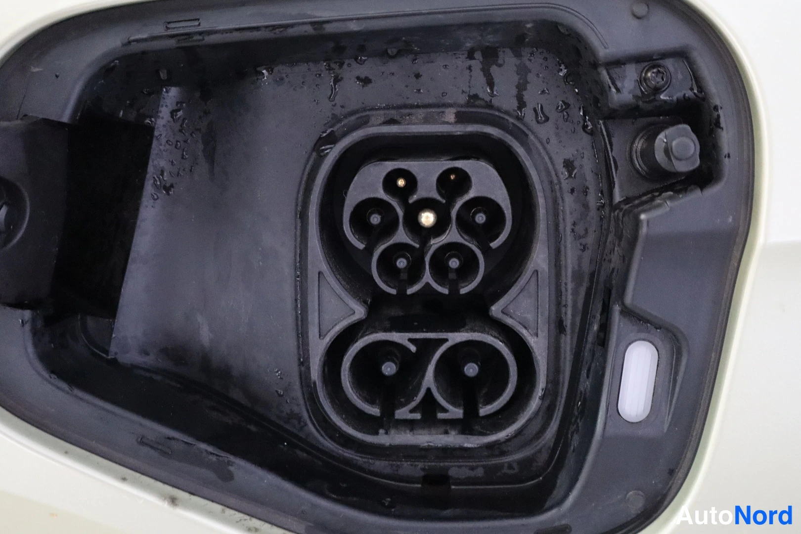 Yksityiskohta: Sähköauton latausliitäntä auki, Combined Charging System -portti pyöreillä kontakteilla, kastunut.
