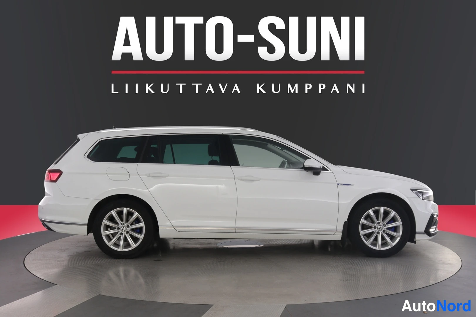 Takaviisto: Valkoinen farmariauto sivuprofiilissa, takavalo ja etuosa näkyvät kulmasta studio-taustaa vasten.