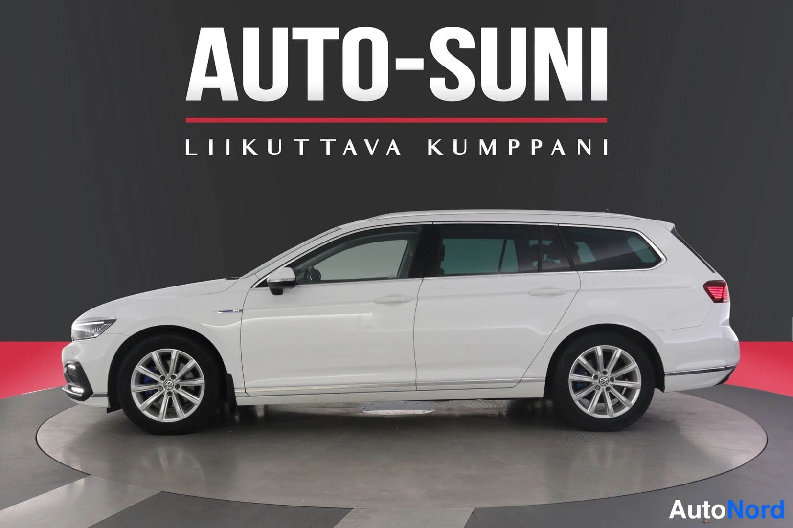 Sivulta: Valkoinen farmariauto sivulta kuvattuna, tumma tausta ja punainen lattia-alue studioympäristössä.