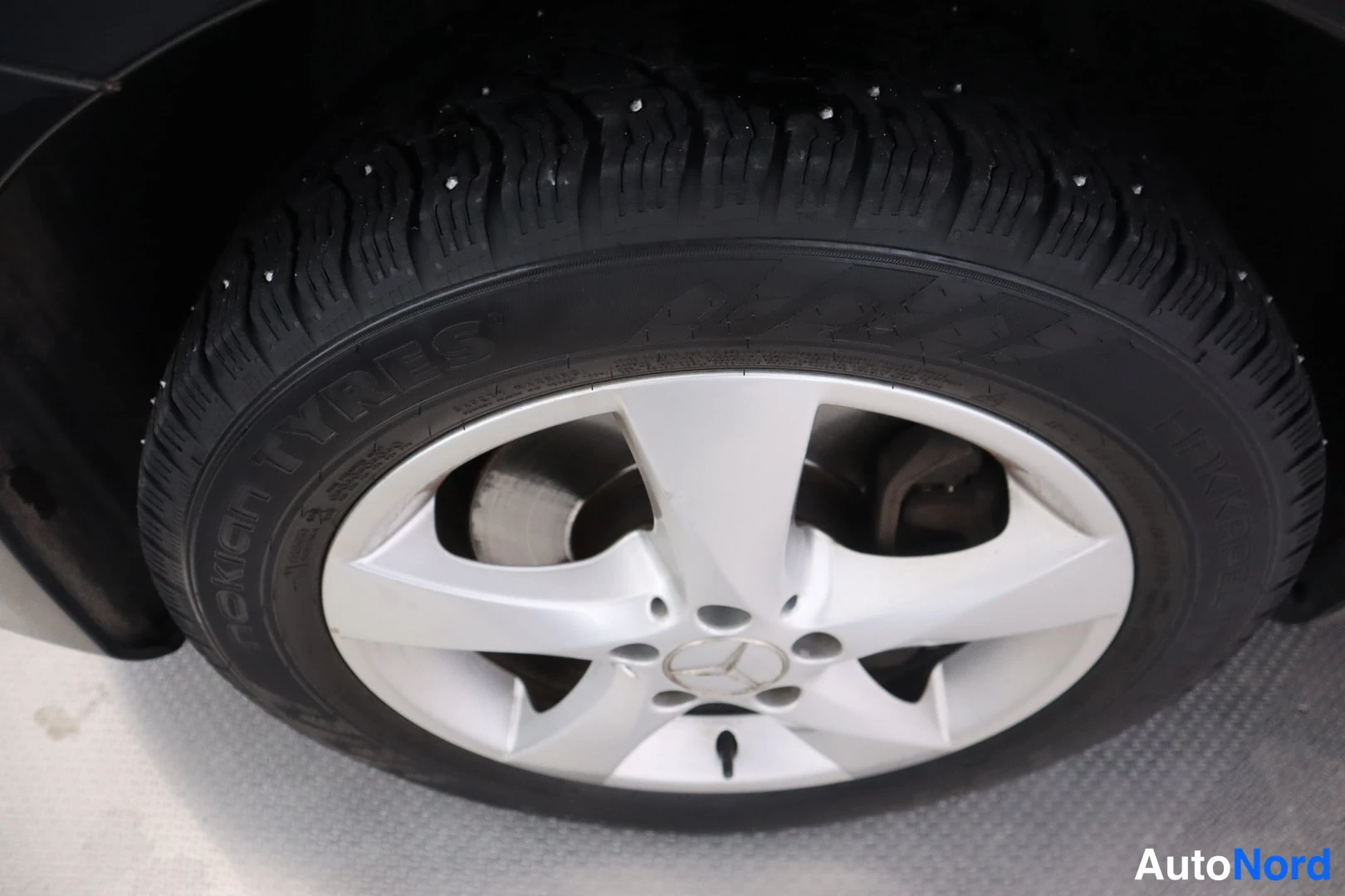 Yksityiskohta: Lähikuva autorenkaasta: hopeavanteessa Mercedes-tähti, nokkanastarenkaita (Nokian Tyres -teksti sivuseinässä).
