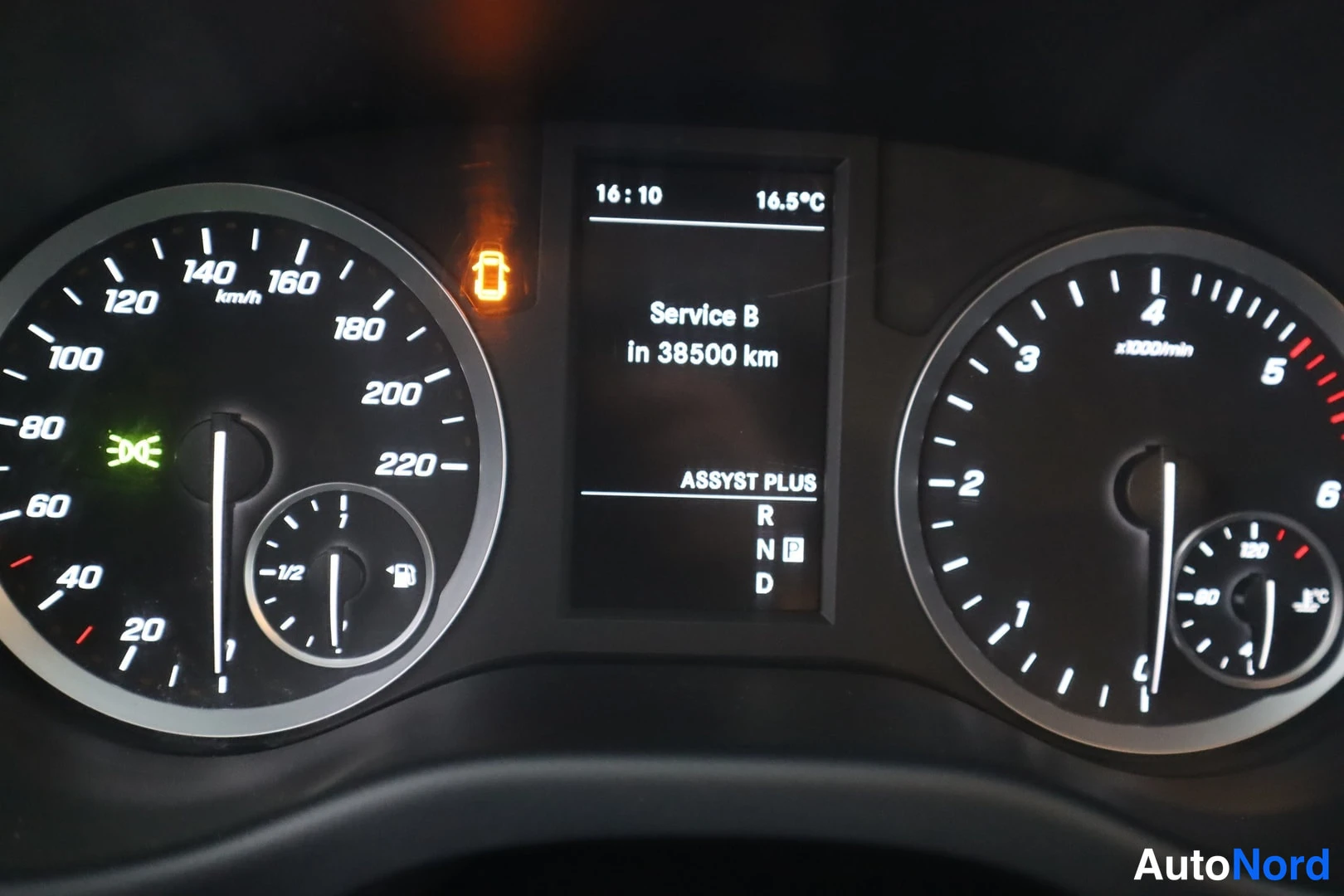 Yksityiskohta: Mittariston lähikuva: nopeus- ja kierrosmittarit, keskellä näyttö tekstillä Service B in 38500 km ja ASSYST PLUS -vaihdetila, sekä päällä oleva huoltovalo.
