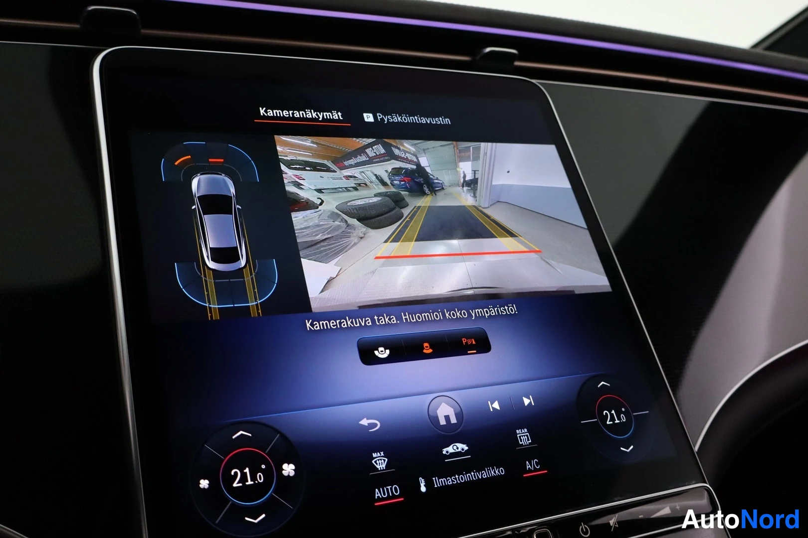 Muu: Auton infotainment-näyttö näyttää kamera Näkymät -toiminnon pysäköintiaustin-kuvaa, jossa on takaosan kamera Näkymä ja pysäköintiväylät.
